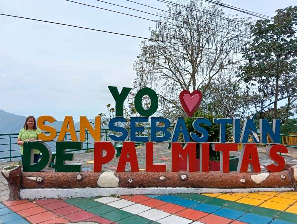 María Luceli Correa junto al emblemático letrero que da apertura a la centralidad de Palmitas desde la vieja carretera al mar./ FOTO: ANDRÉS BEDOYA.